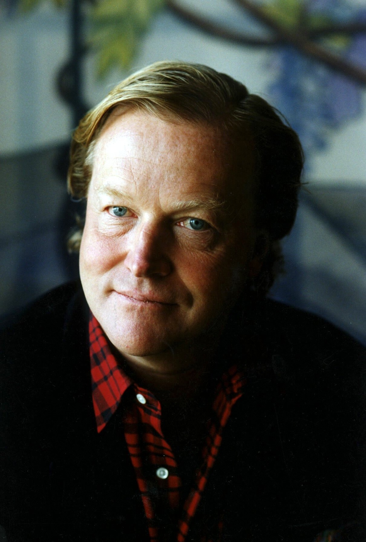 Porträttfoto av en man i röd rutig skjorta mot en suddig bakgrund.