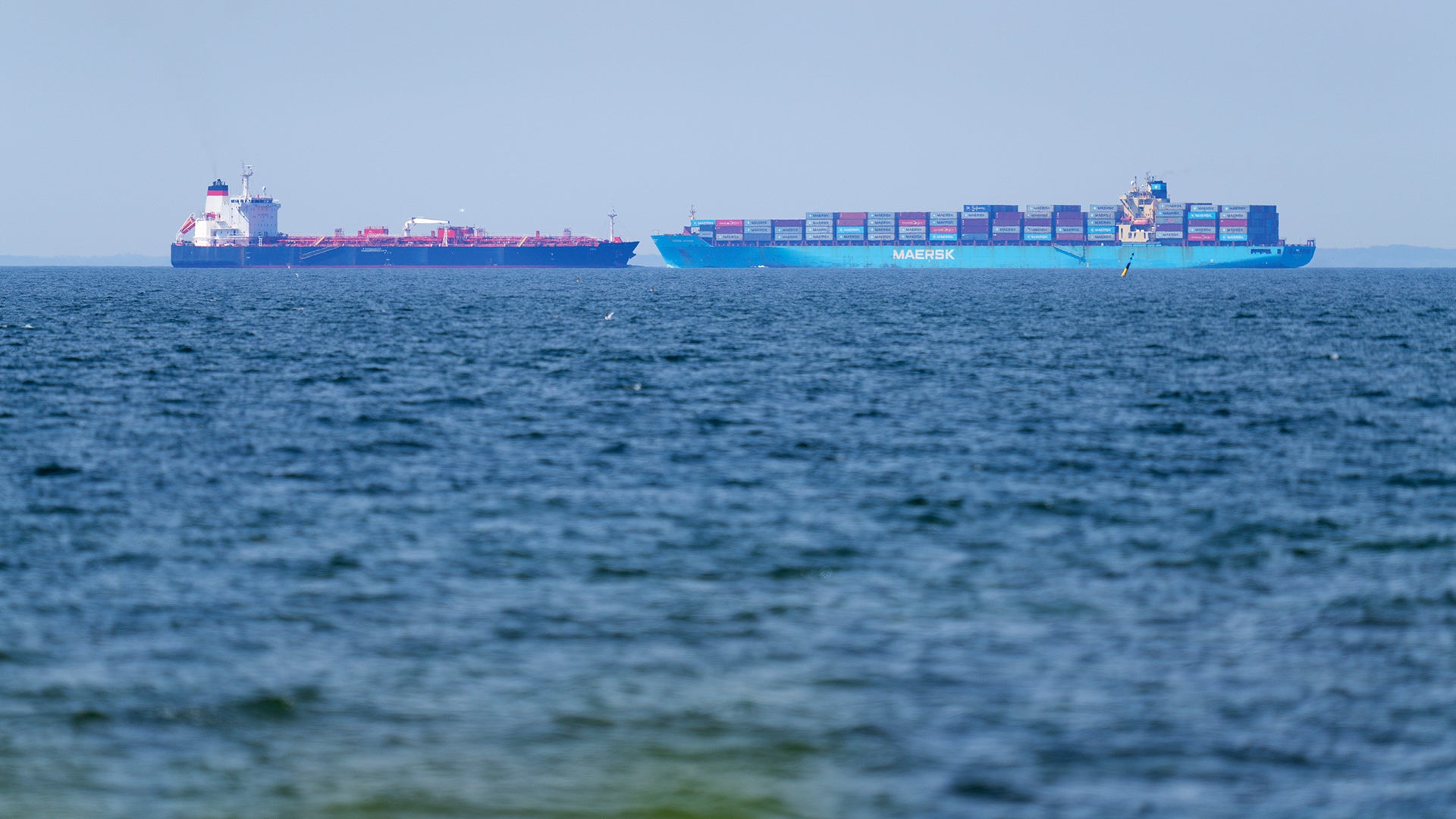 Ett stort blått containerfartyg lastat med färgade containerboxar ligger på öppet hav.