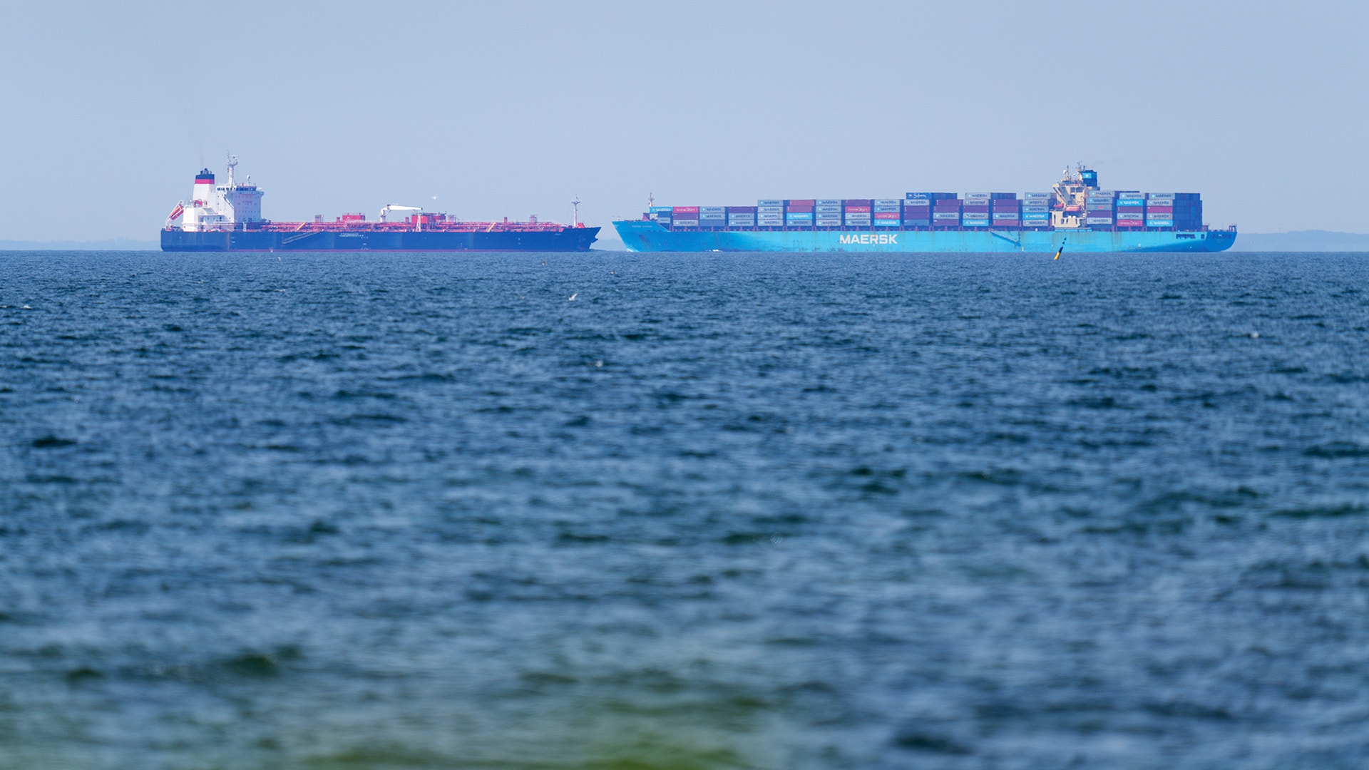 Ett stort blått containerfartyg lastat med färgade containerboxar ligger på öppet hav.