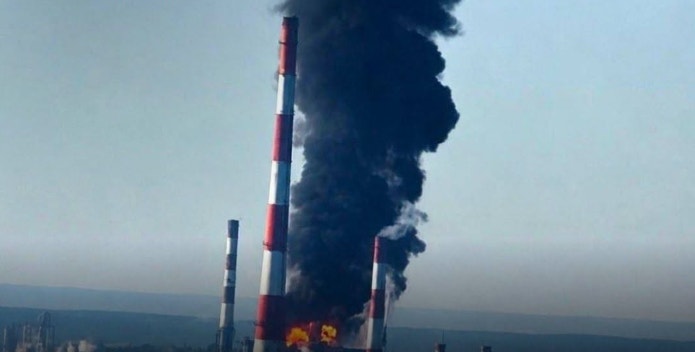 Industriell skorsten med röd och vit färgning som släpper ut tjock svart rök från en brand.