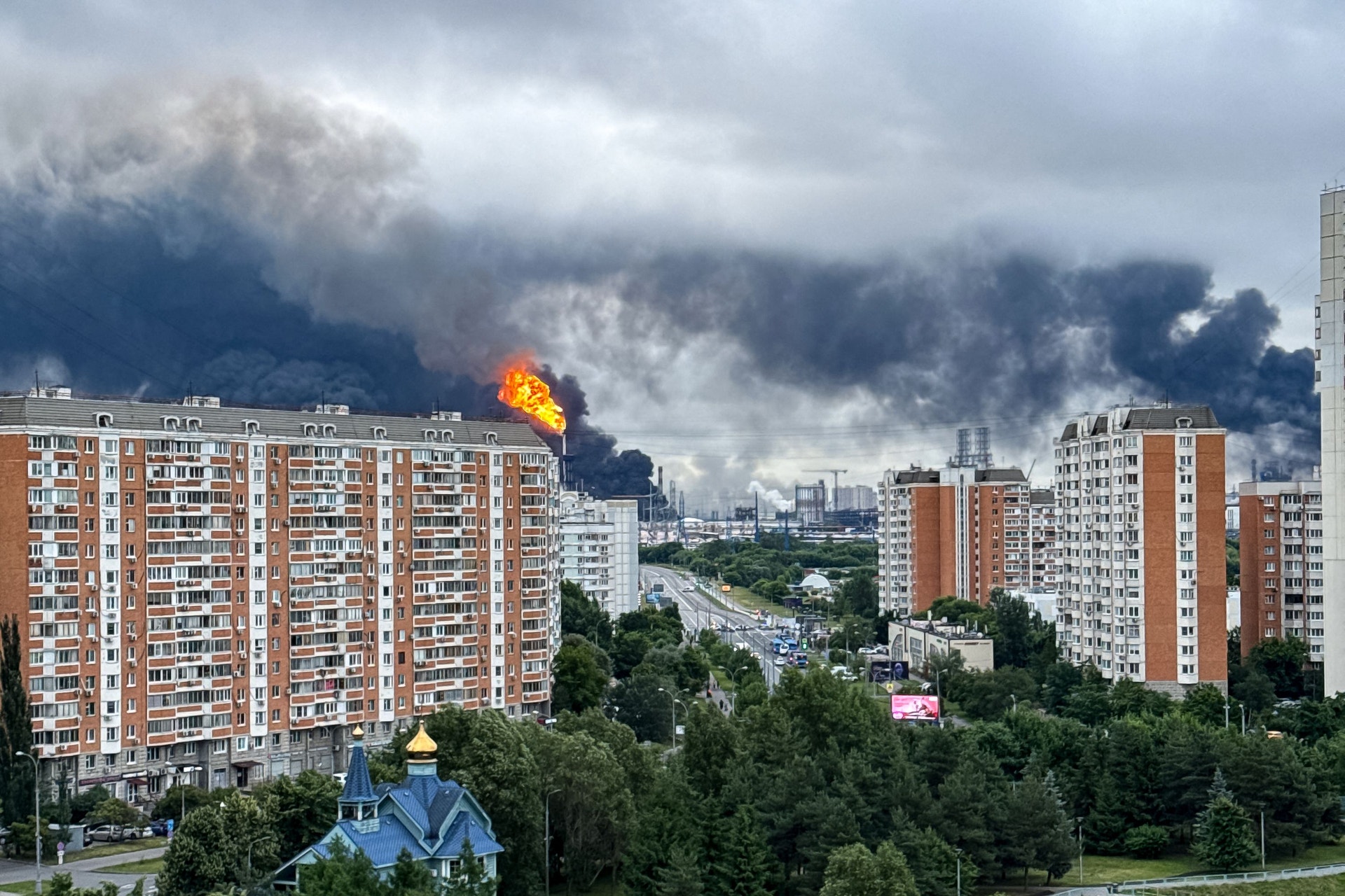 Stadsvy med flerbostadshus och en explosion med svart rök och lågor i fjärran