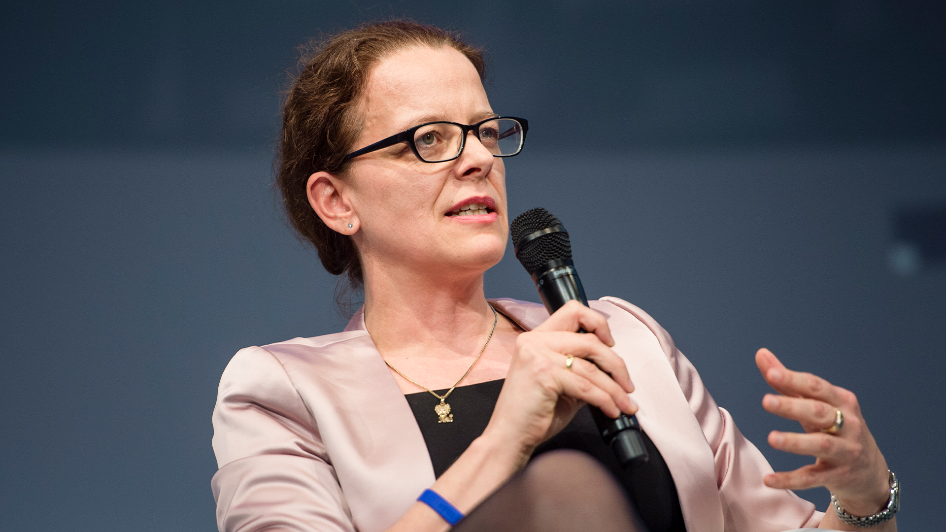 Porträttfoto av en kvinna som talar vid ett podium med mikrofon.