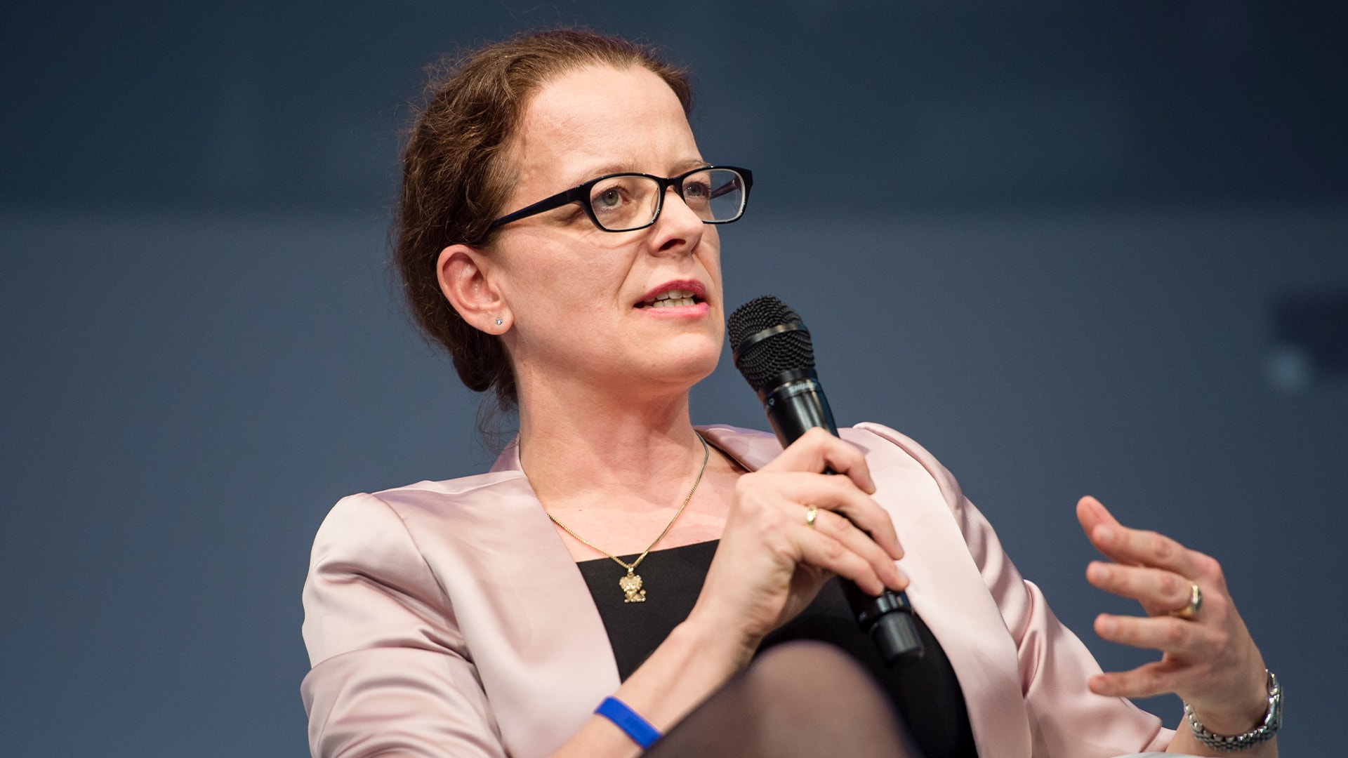 Porträttfoto av en kvinna som talar vid ett podium med mikrofon.