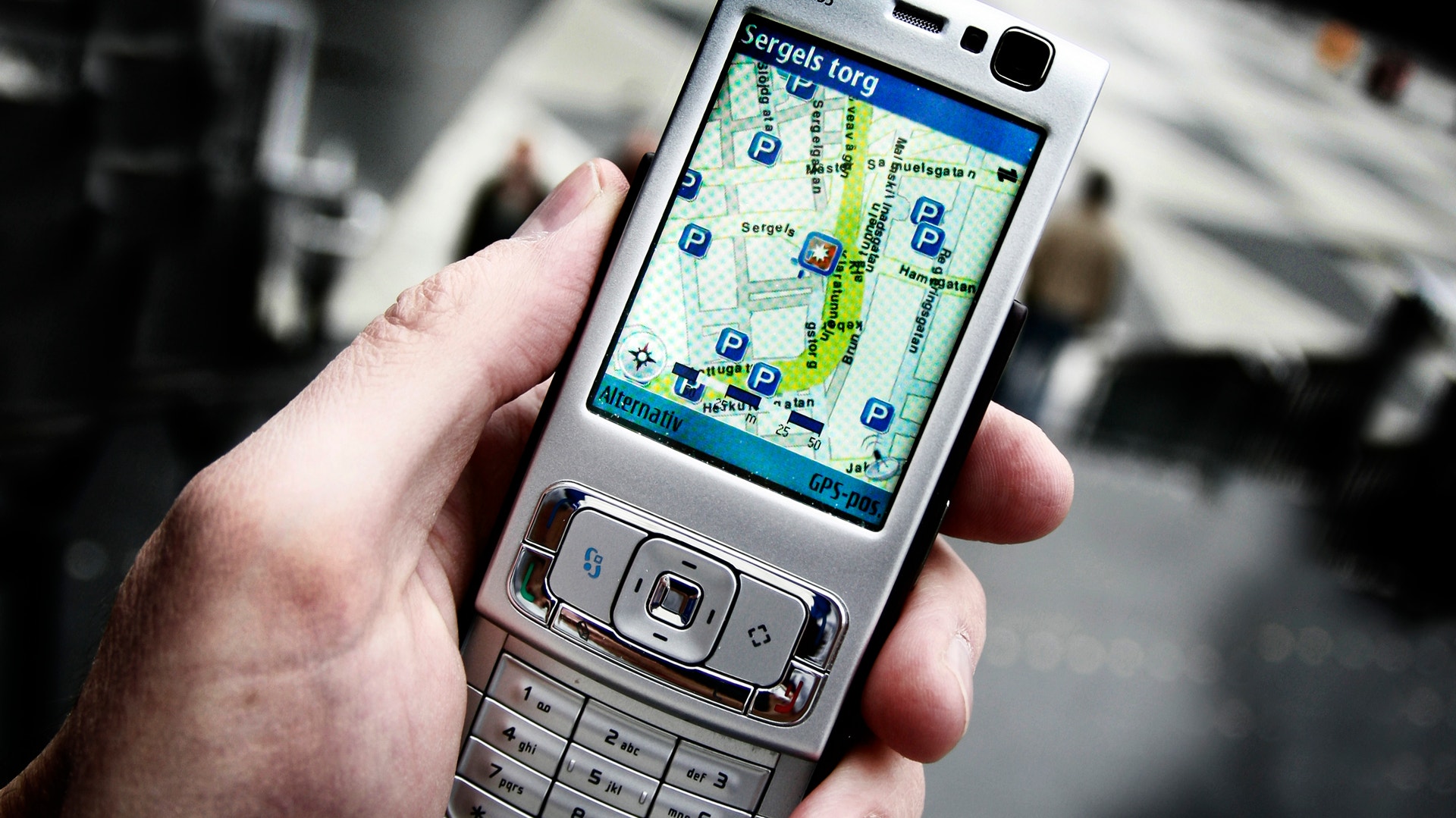 En hand håller en äldre mobiltelefon som visar en karta på skärmen.