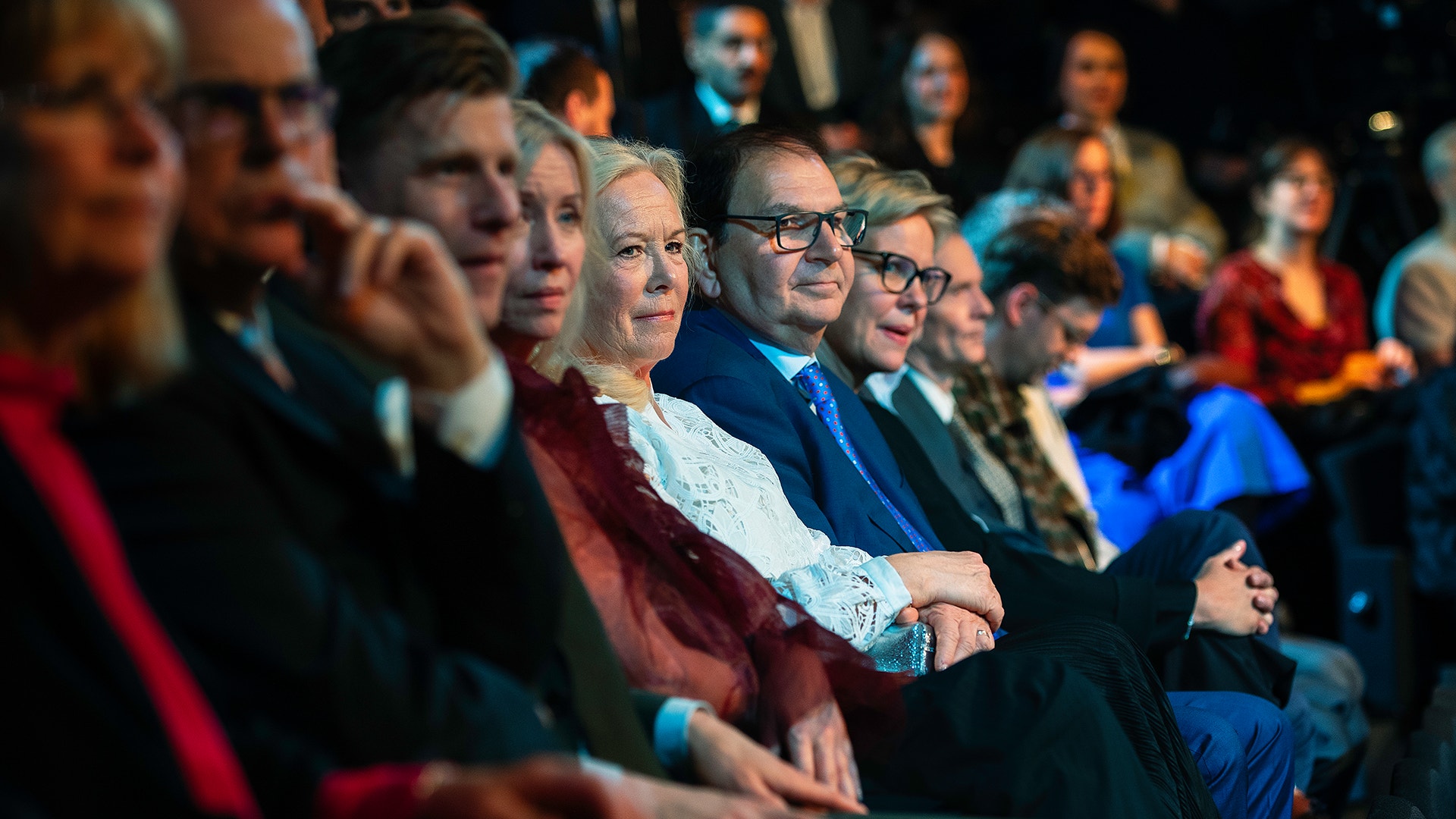 En grupp människor i formell klädsel sitter tillsammans och tittar på ett evenemang eller en föreställning.