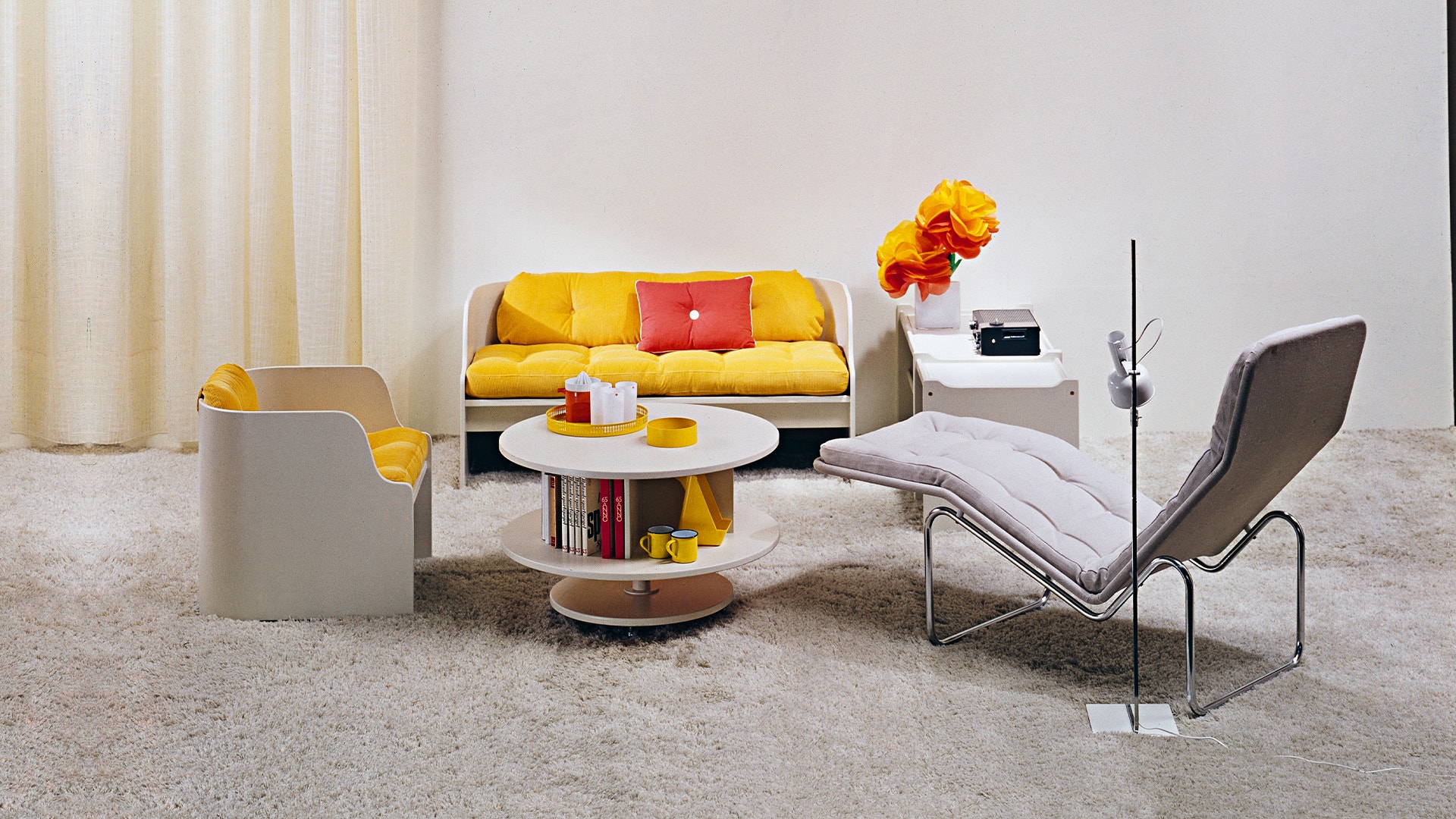 Modernt vardagsrum med gul och röd soffa, grå fåtölj, vit soffbord och minimalistisk inredning