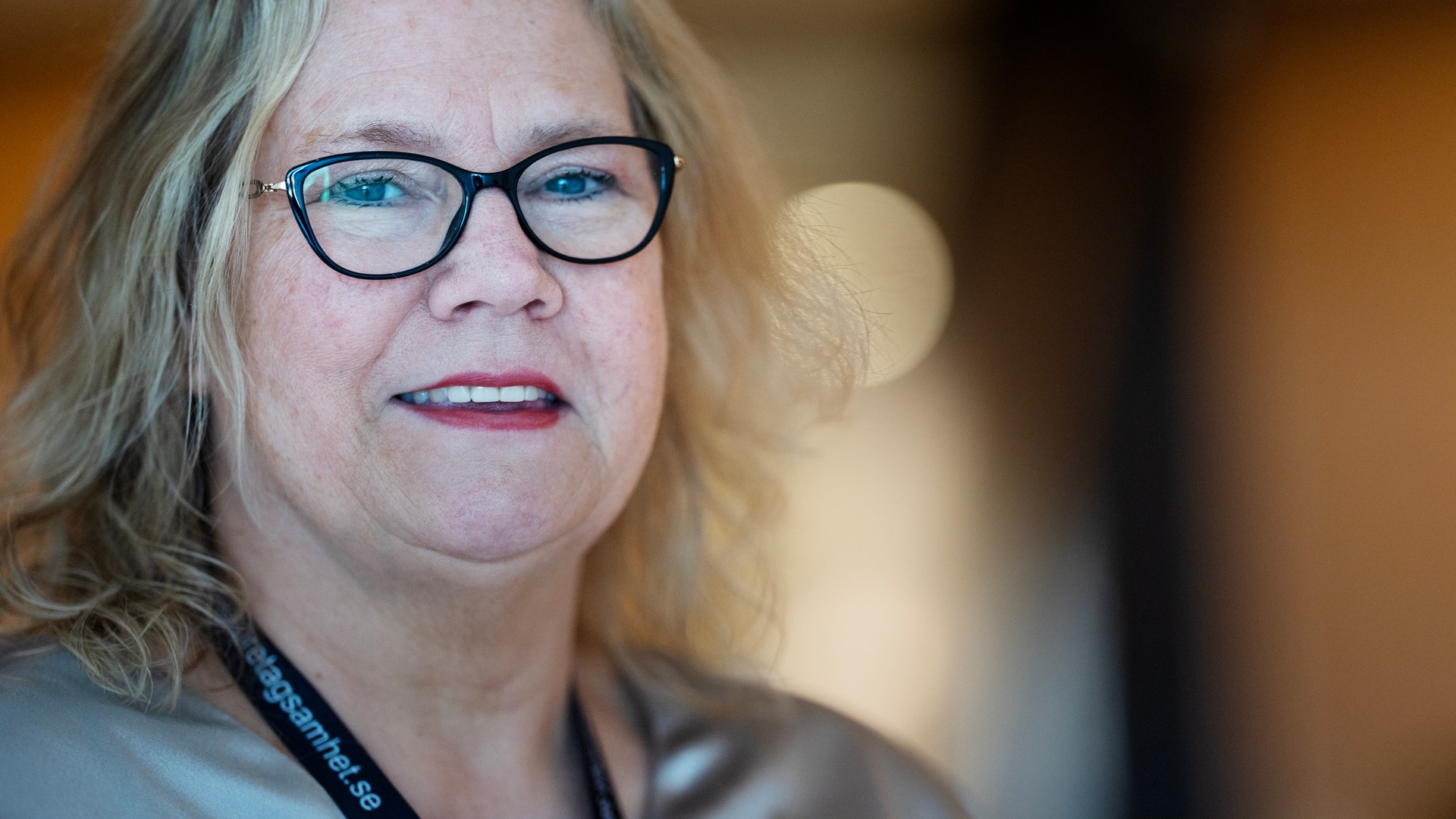 Porträtt av en kvinna med glasögon och långt gråblont hår som ler mot kameran.