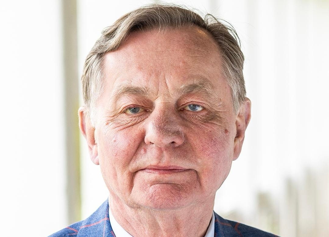 Porträtt av en man i blå skjorta mot en neutral bakgrund.