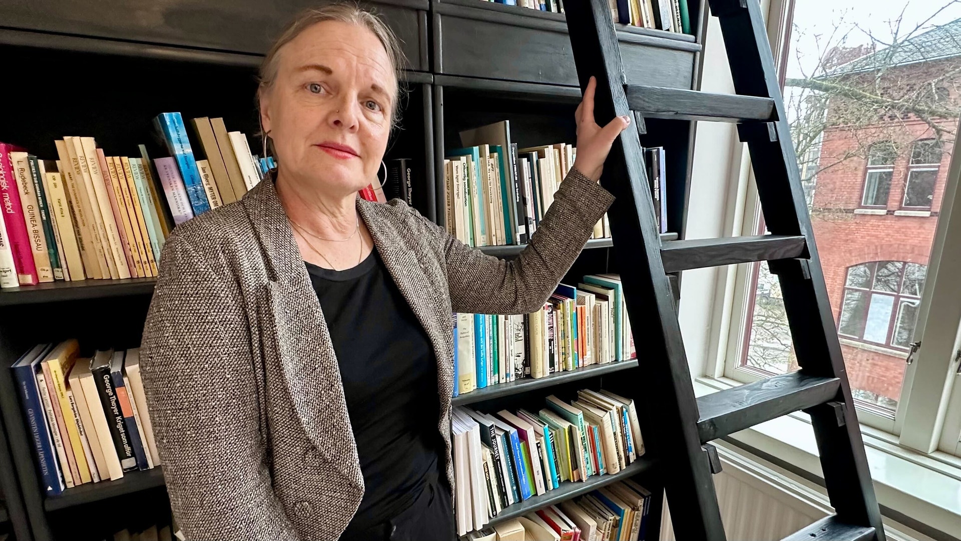Isabell Schierenbeck vid Göteborgs universitet står vid en svart bokhylla med stege inomhus.