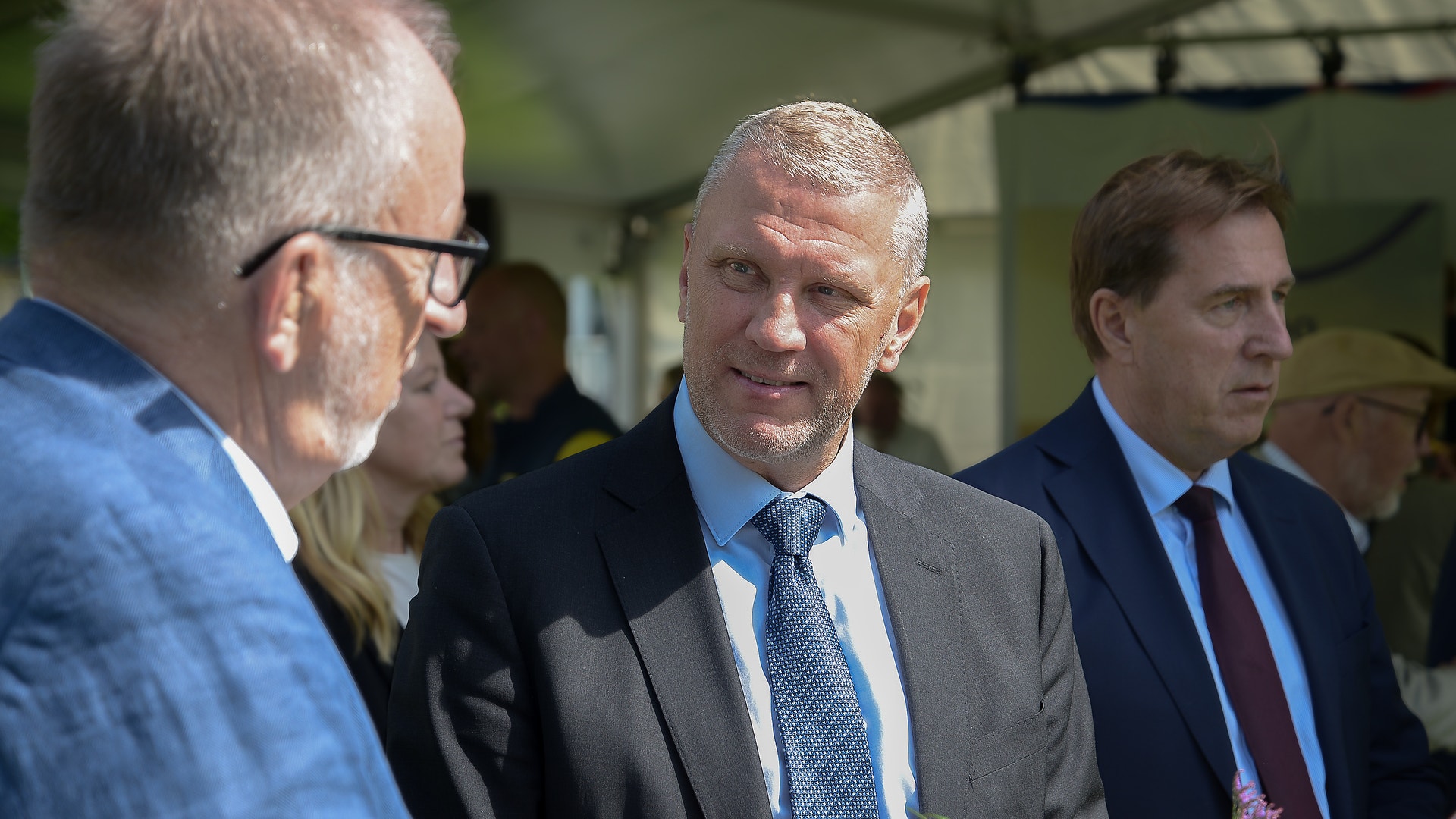 Flera män i affärskläder samtalar tillsammans vid ett formellt evenemang inomhus.
