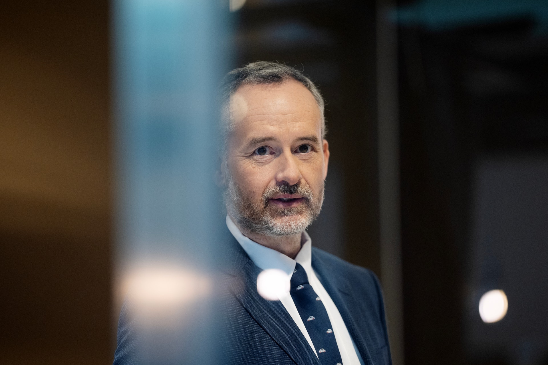 Porträtt av en man i kostym och slips mot en suddig bakgrund.