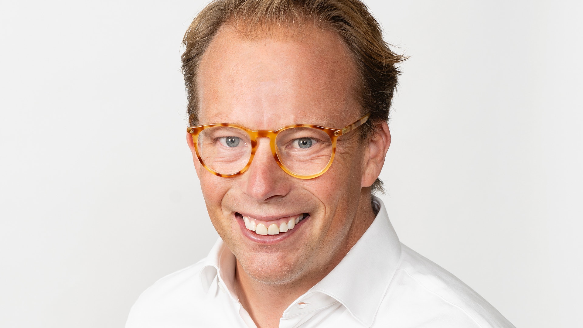 Porträttfoto av en man med orangeglasögon och vit skjorta mot ljus bakgrund