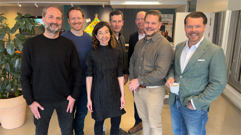 Gruppfoto med sex personer som står tillsammans i ett modernt kontorsutrymme.