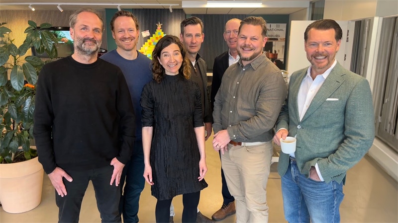 Gruppfoto med sex personer som står tillsammans i ett modernt kontorsutrymme.