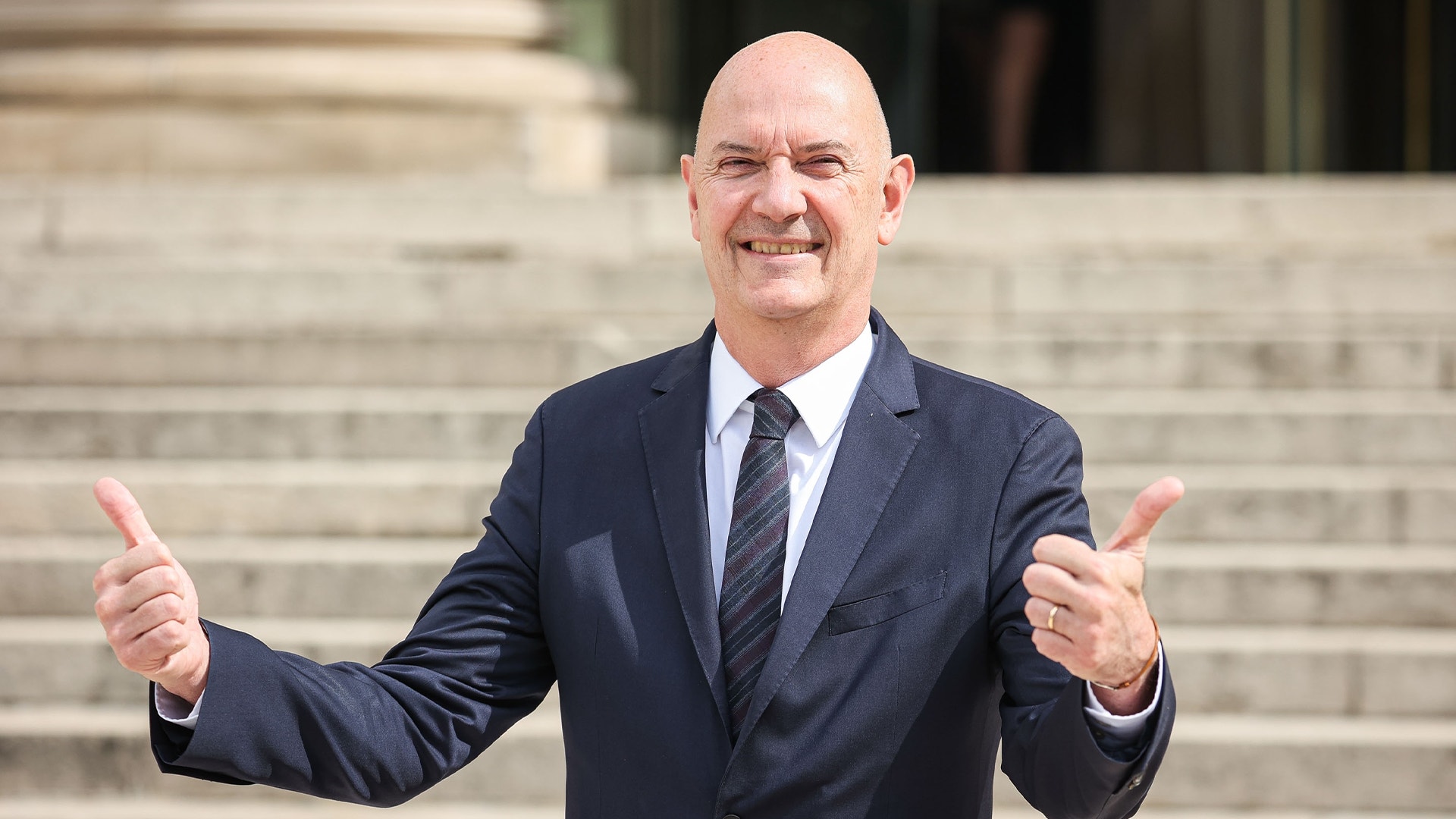 Man i kostym ger två tummar upp framför en stentrap