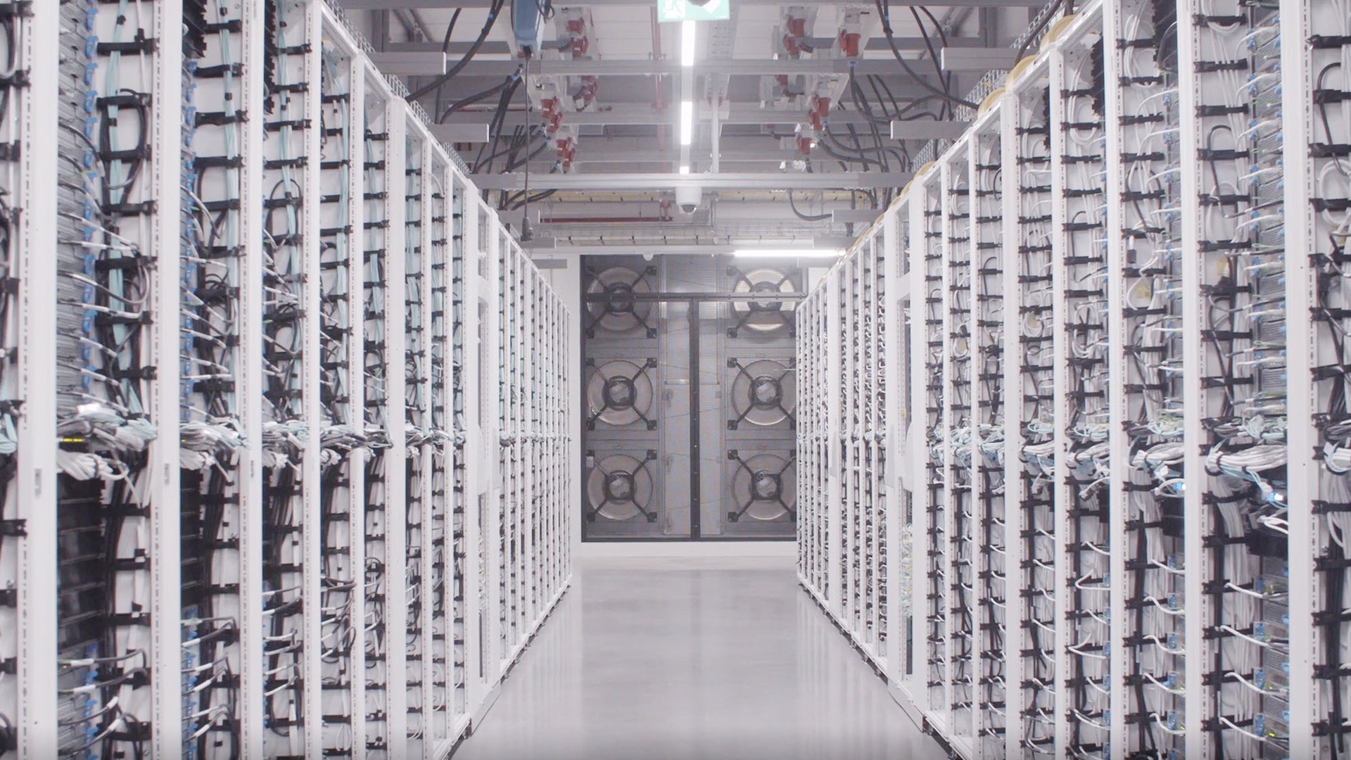 Gång mellan rader av serverskåp i ett datacenter, med stora kylfläktar längre bort.
