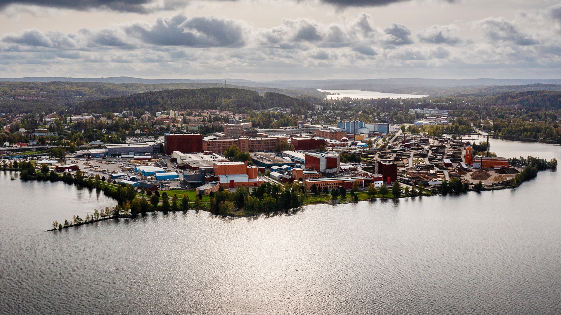 Flygbild över en industrianläggning vid en sjö, omgiven av skog.