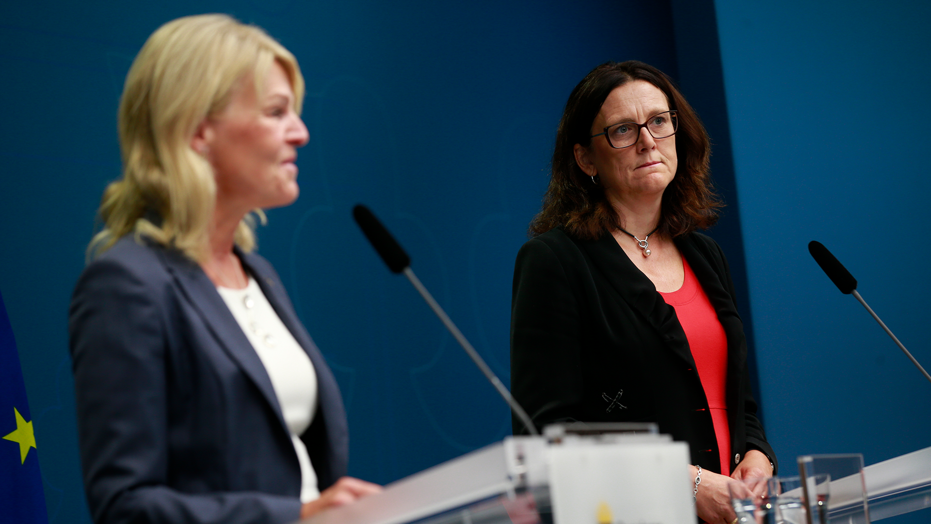 Två kvinnor vid ett podium under en presskonferens med blå bakgrund.