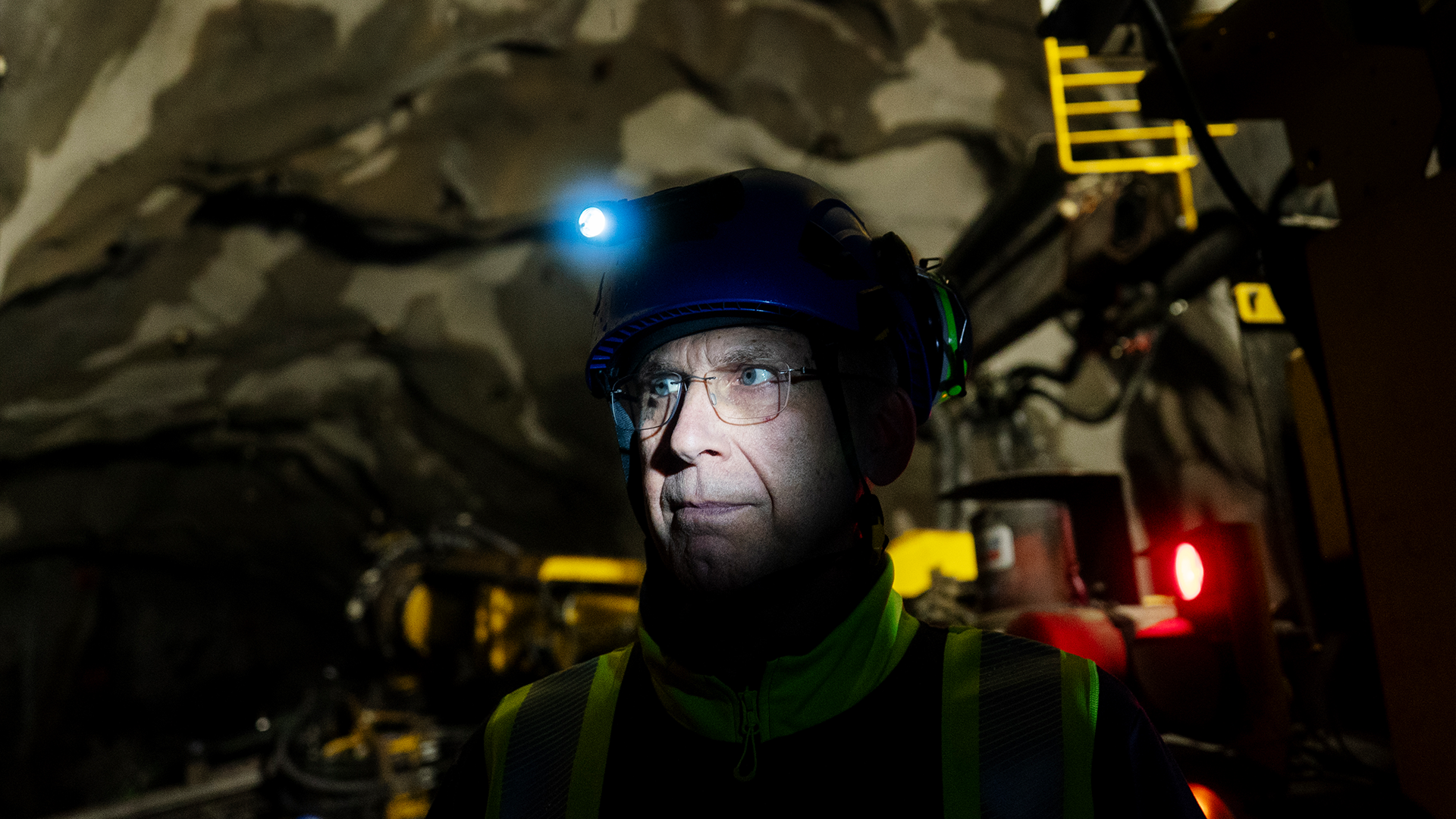 En person i säkerhetsutrustning med hjälm och pannlampa i en underjordisk miljö.