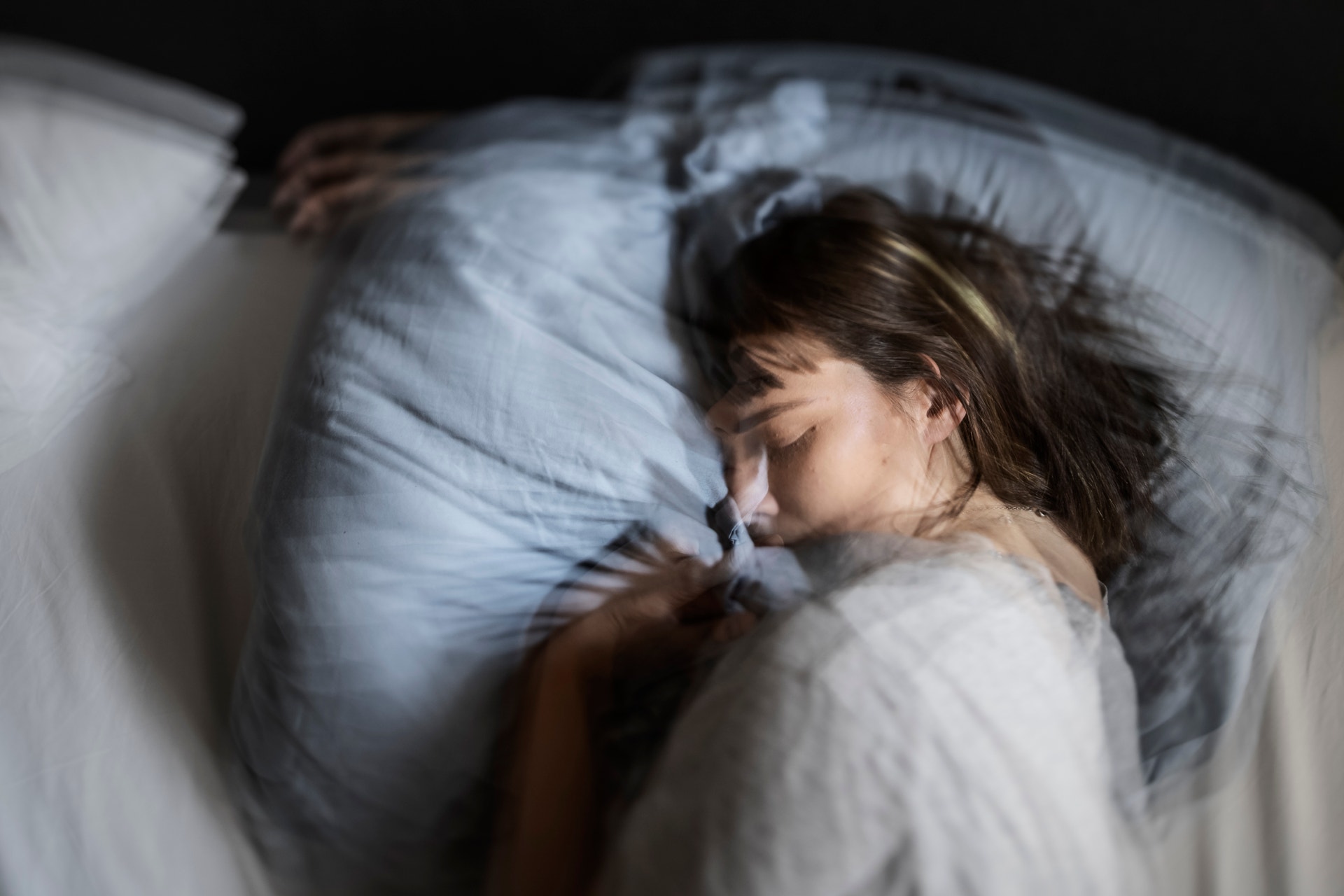 En kvinna ligger och sover i en säng med ljusblå kuddar och täcke.