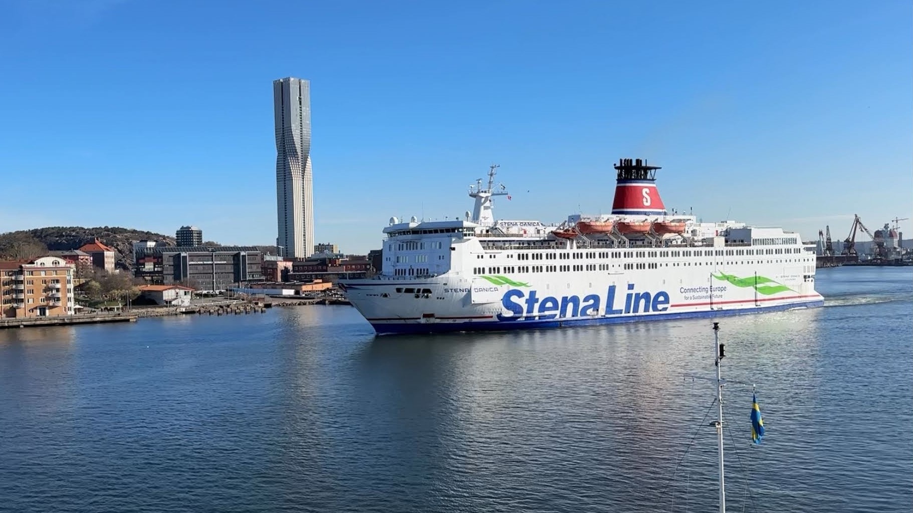 En vit färja från Stena Line passerar i Göteborgs hamn och i bakgrunden syns den höga byggnaden Karlatornet, under blå himmel.