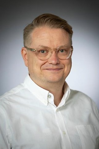Porträttbild av en man med glasögon och vit skjorta mot grå bakgrund.