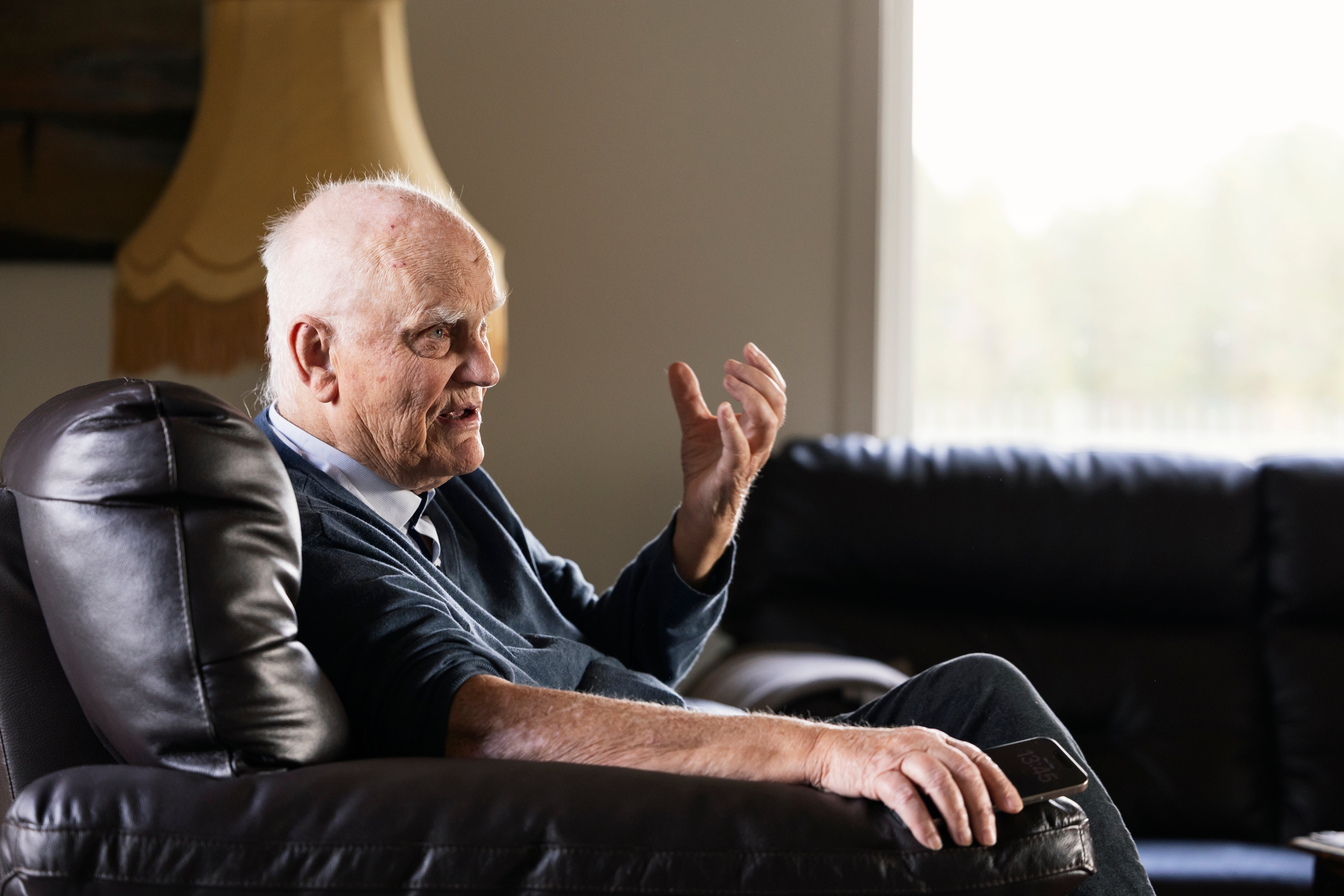 En äldre man sitter i en svart lädersstol och gestikulerar medan han talar.