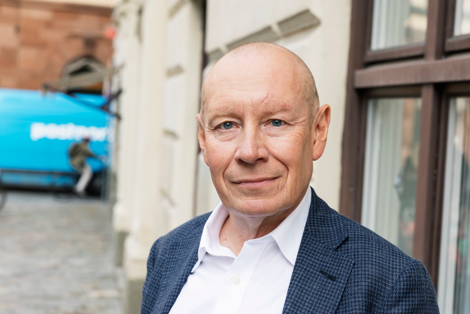 Porträtt av en man i mörkblå kavaj och vit skjorta som står utanför en byggnad och ler mot kameran.
