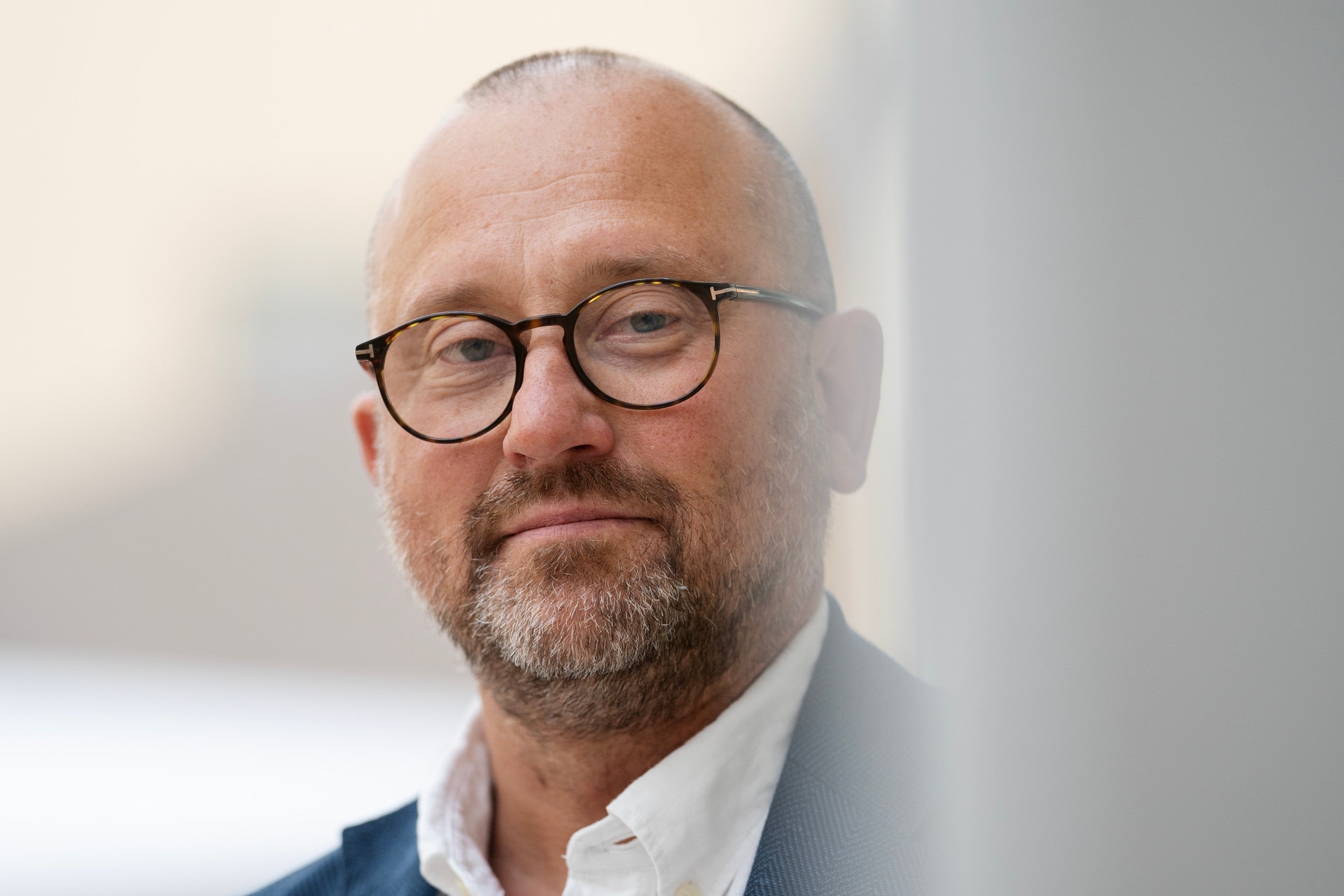 Porträtt av en man med glasögon och skägg, klädd i blazer och vit skjorta.
