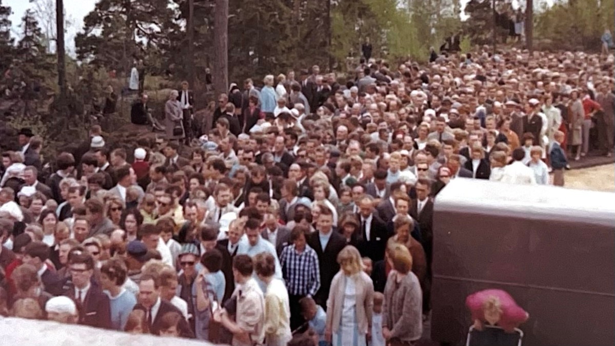 Stor folksamling vid en invigning 1965. Många människor i formell klädsel står tätt tillsammans utomhus framför träd.
