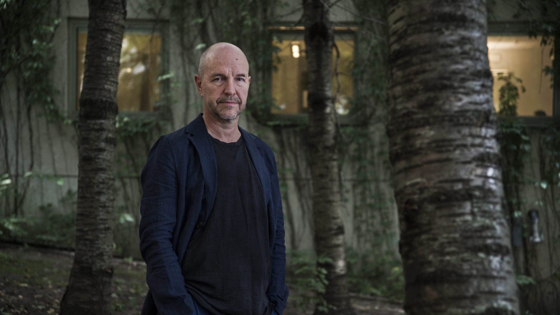 Porträttfoto av en man som står bland palmträd framför en byggnad.