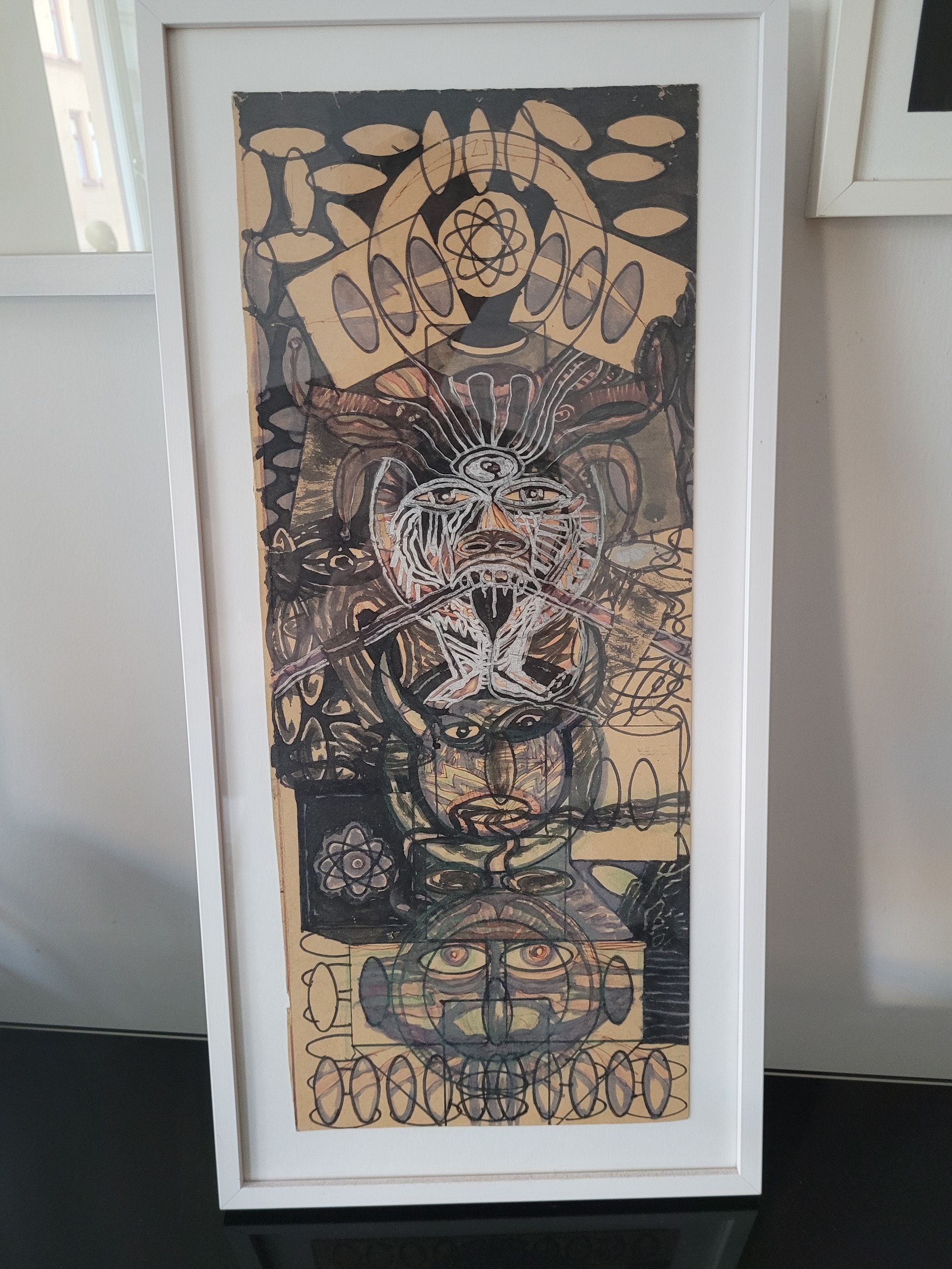 Abstrakt konstverk i svart och beige med surrealistiska motiv, organiska former och ansiktsliknande figurer arrangerade vertikalt i en vit ram.