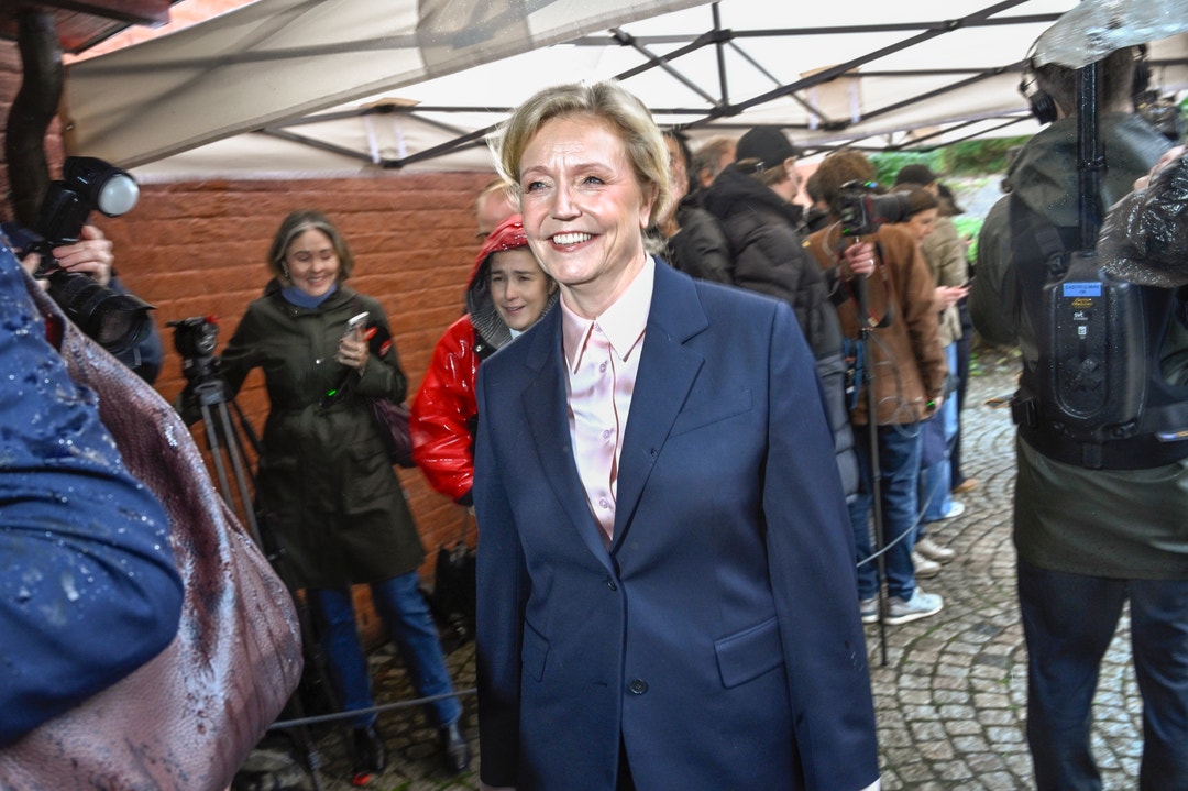 Elisabeth Thand Ringqvist, partiledare för Centerpartiet, ler när hon går utomhus i regn, omgiven av fotografer och journalister.