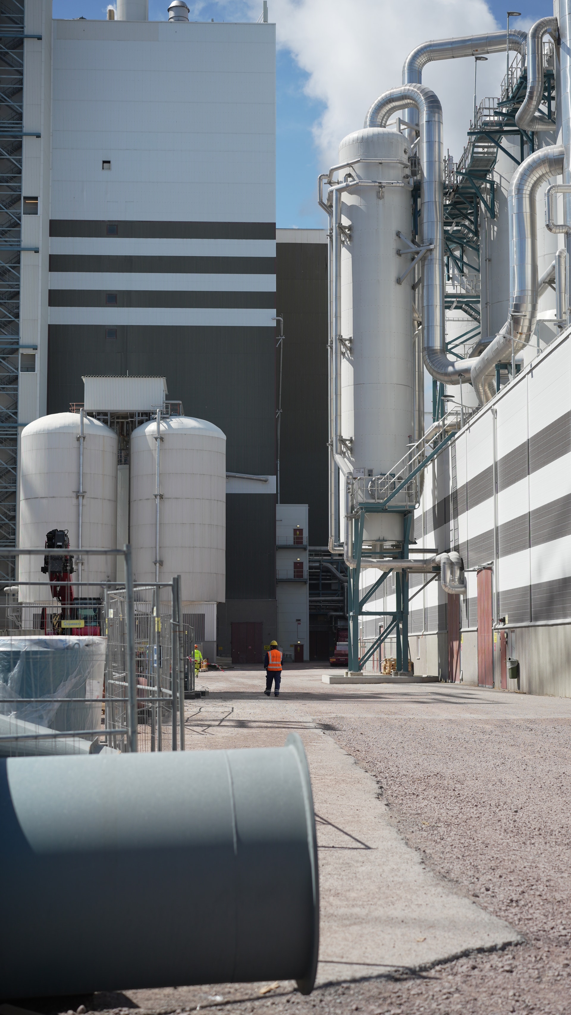 Industriell anläggning med stora metallbehållare, rör och en byggnad i bakgrunden.