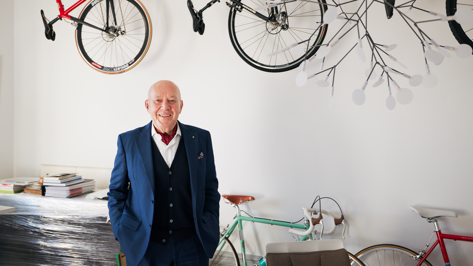 Porträtt av en man i blå kavaj omgiven av cyklar i en cykelbutik