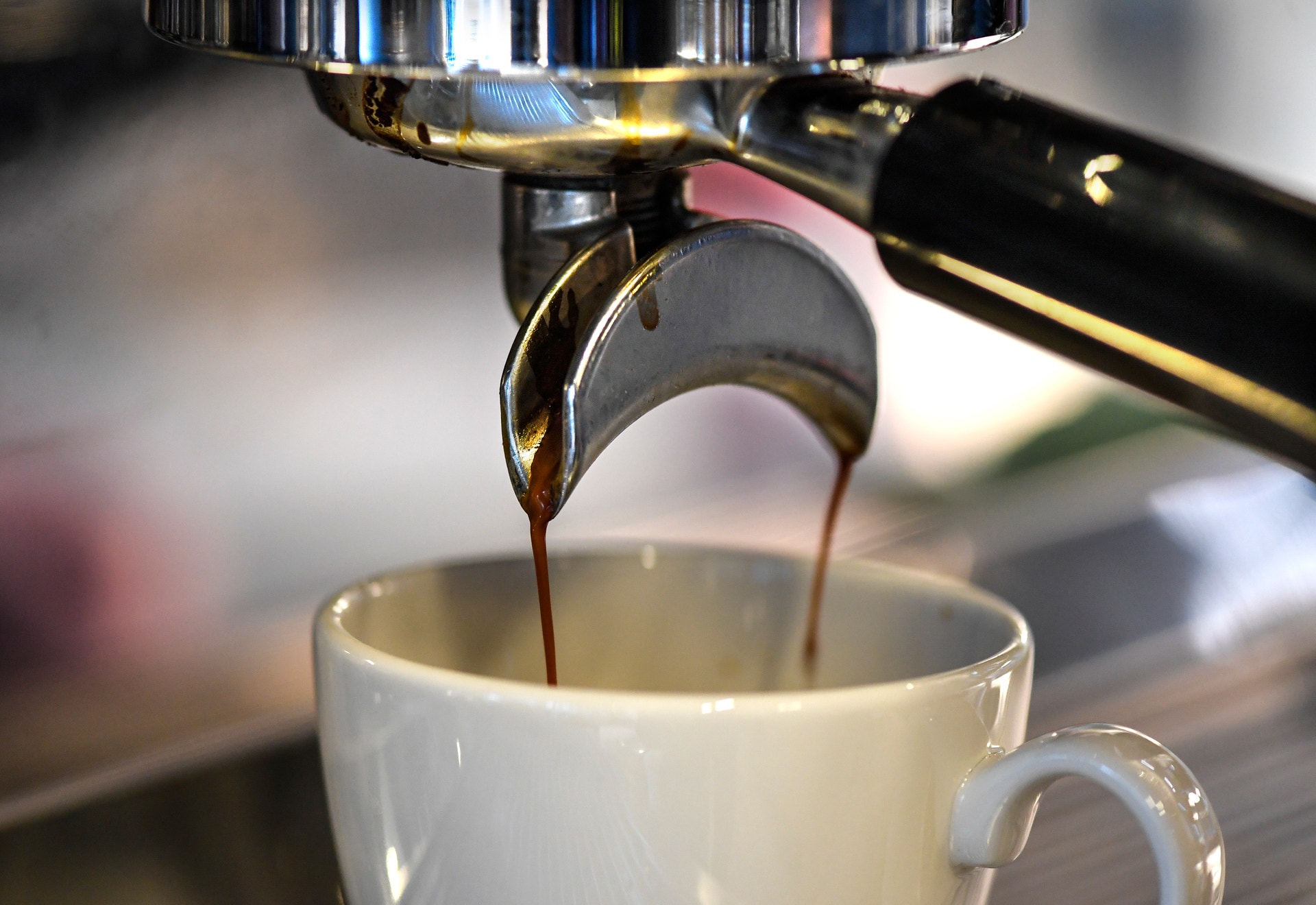 Espressomaskine häller mörkt kaffe i en vit kopp