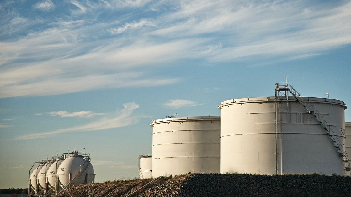 Stora vita lagertankar vid en raffinaderi under blå himmel med moln.