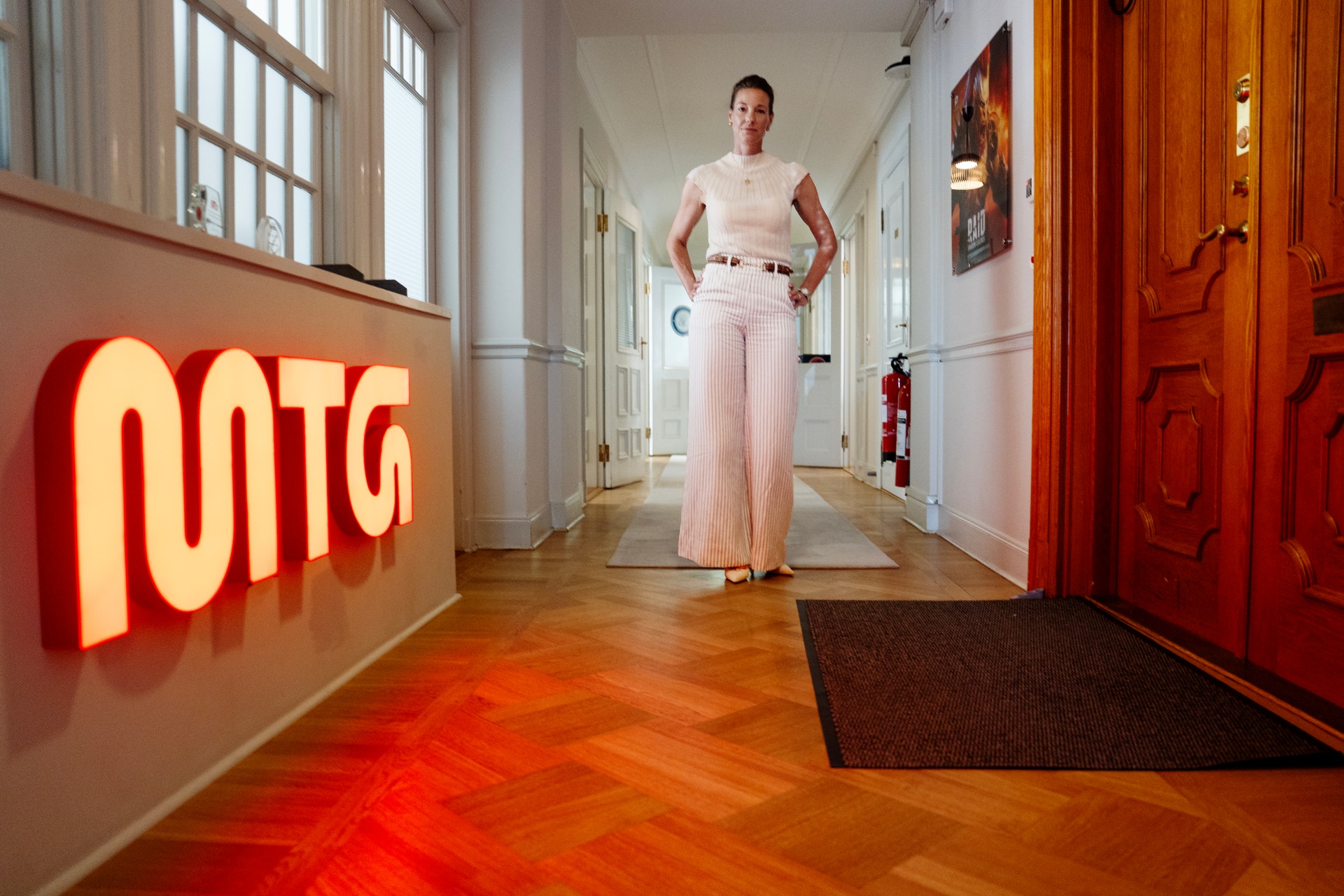 Kvinna i ljusa kläder står i en hallway med ett rött neonskylte bakom sig.