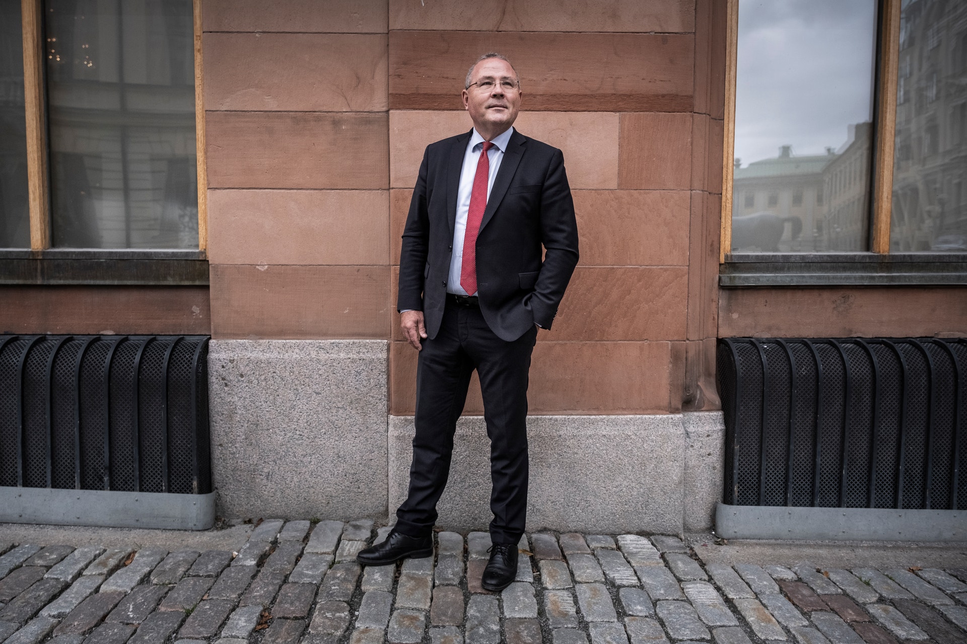En man i kostym med slips står utomhus framför en stenbyggnad.