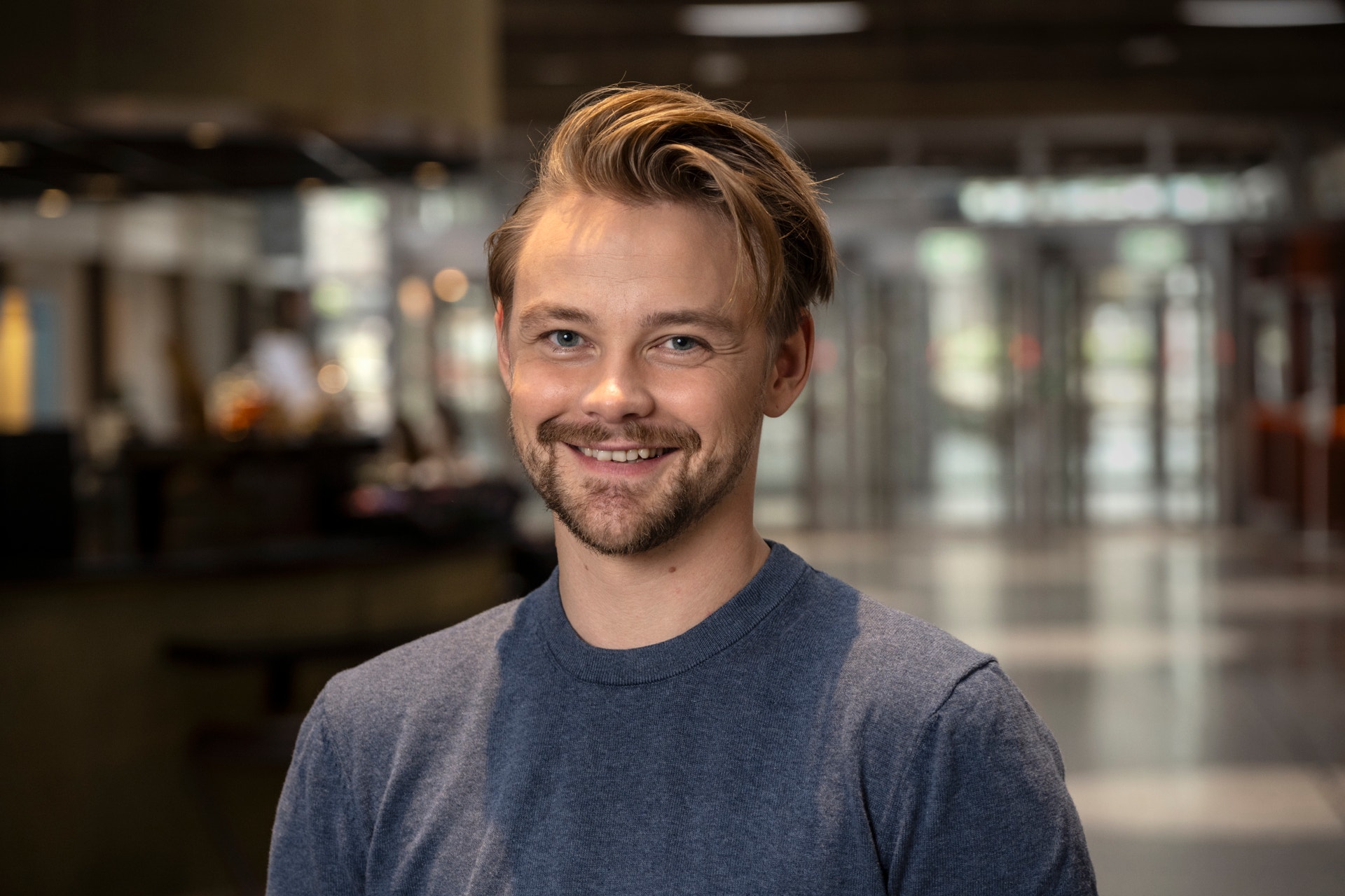 Hampus Hedström står i en gråblå tröja och tittar in i kameran leendes.