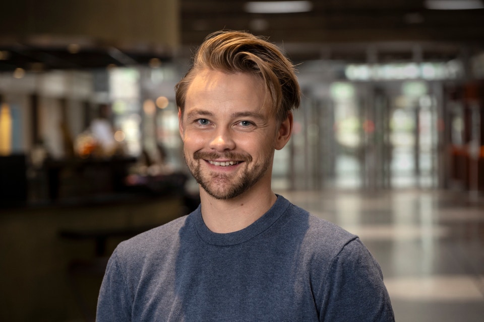 Hampus Hedström står i en gråblå tröja och tittar in i kameran leendes.