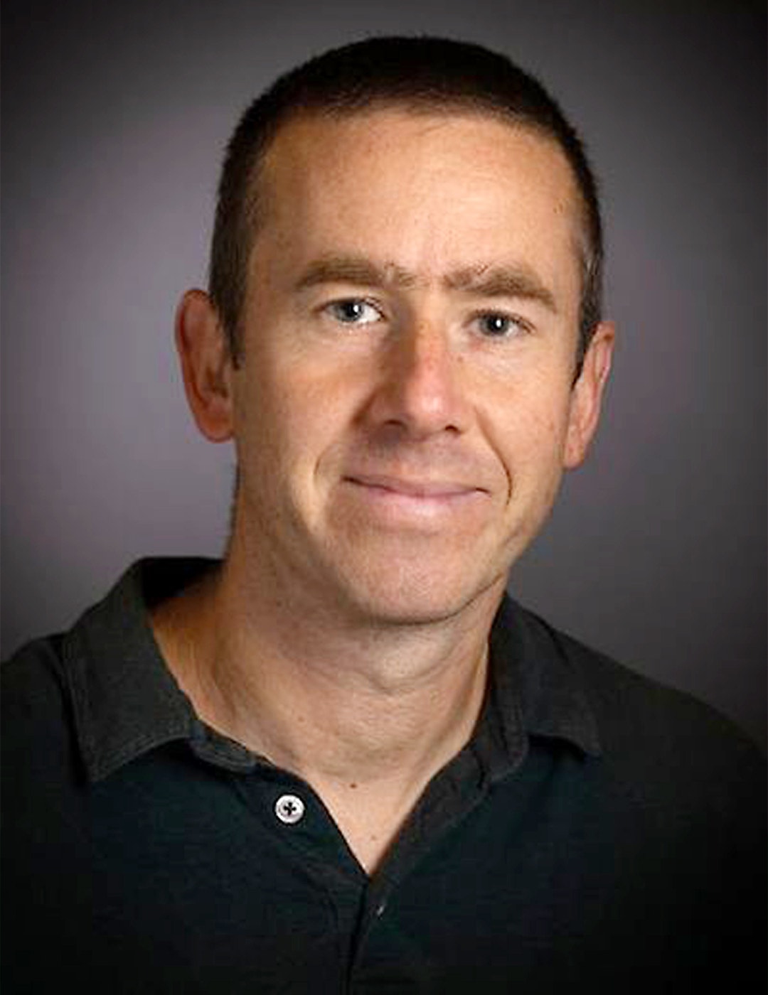 Porträttfoto av en man i svart skjorta mot neutral bakgrund