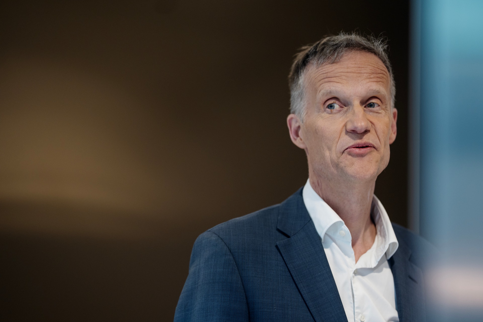 Porträtt av en man i kostym och vit skjorta mot en suddig bakgrund.