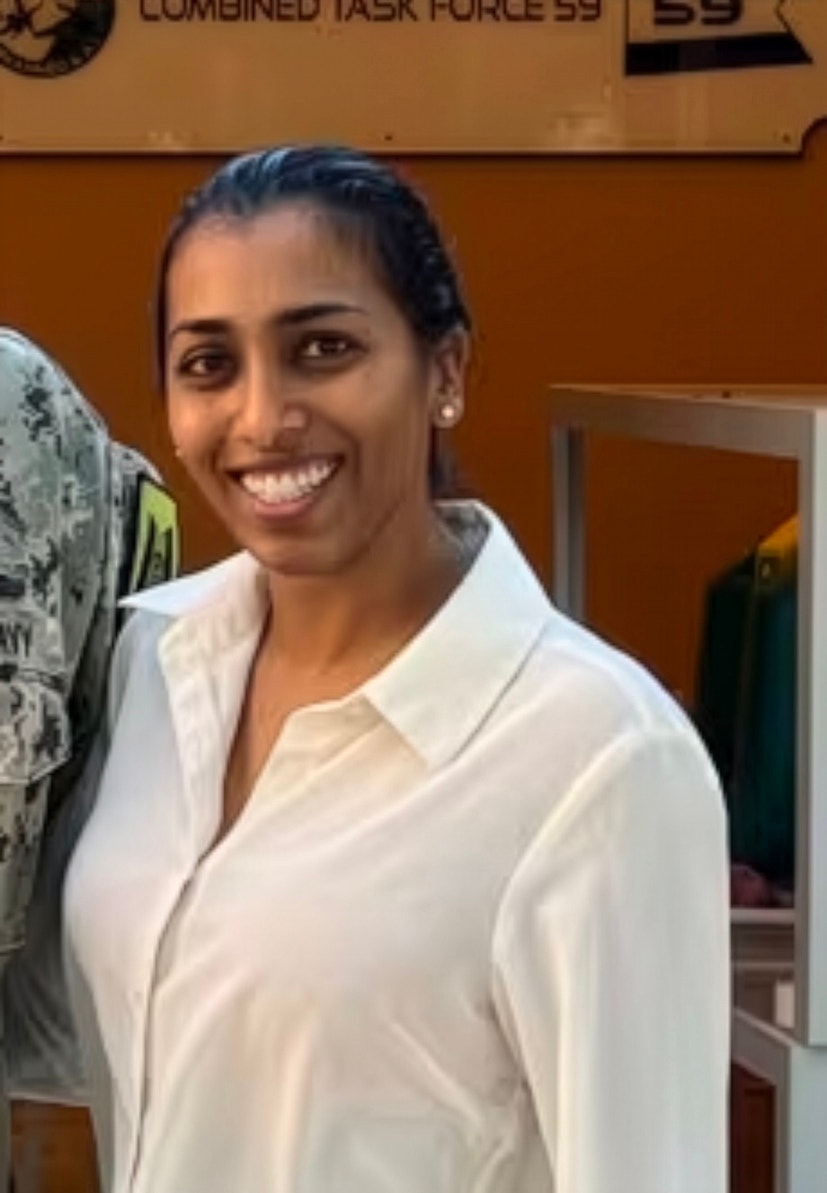 Porträttfoto av en leende kvinna i vit skjorta framför en orange vägg inomhus.