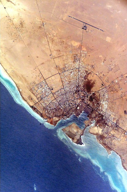 Flygfoto från ovan över Yanbu, en kuststad i Saudiarabien. Bilden visar bebyggelsen längs stranden, öknen runt omkring och det blå havet med vita vågor.