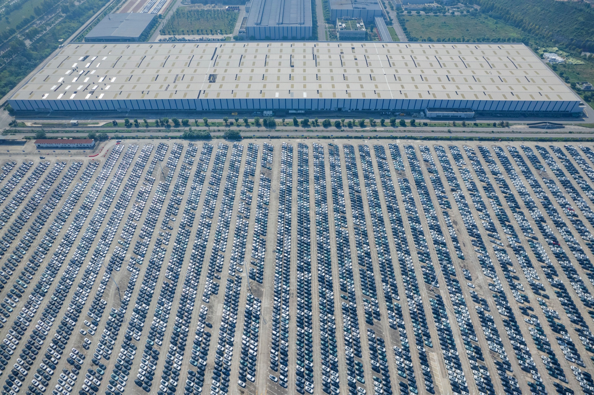 Flygfoto över en stor industrianläggning med el- och hybridbilar i förgrunden och ett stort lagerbyggnad i bakgrunden.