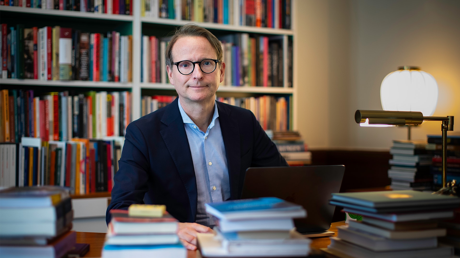  Lars Strannegård vid ett skrivbord framför en stor hylla med böcker.