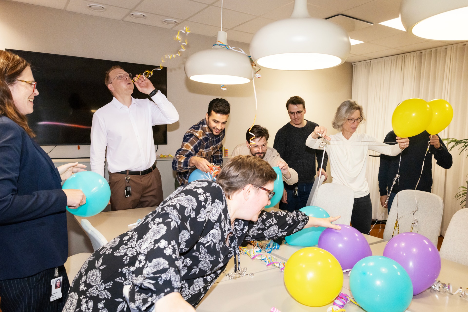 Glada kollegor firar med ballonger och konfetti i ett kontorsrum.
