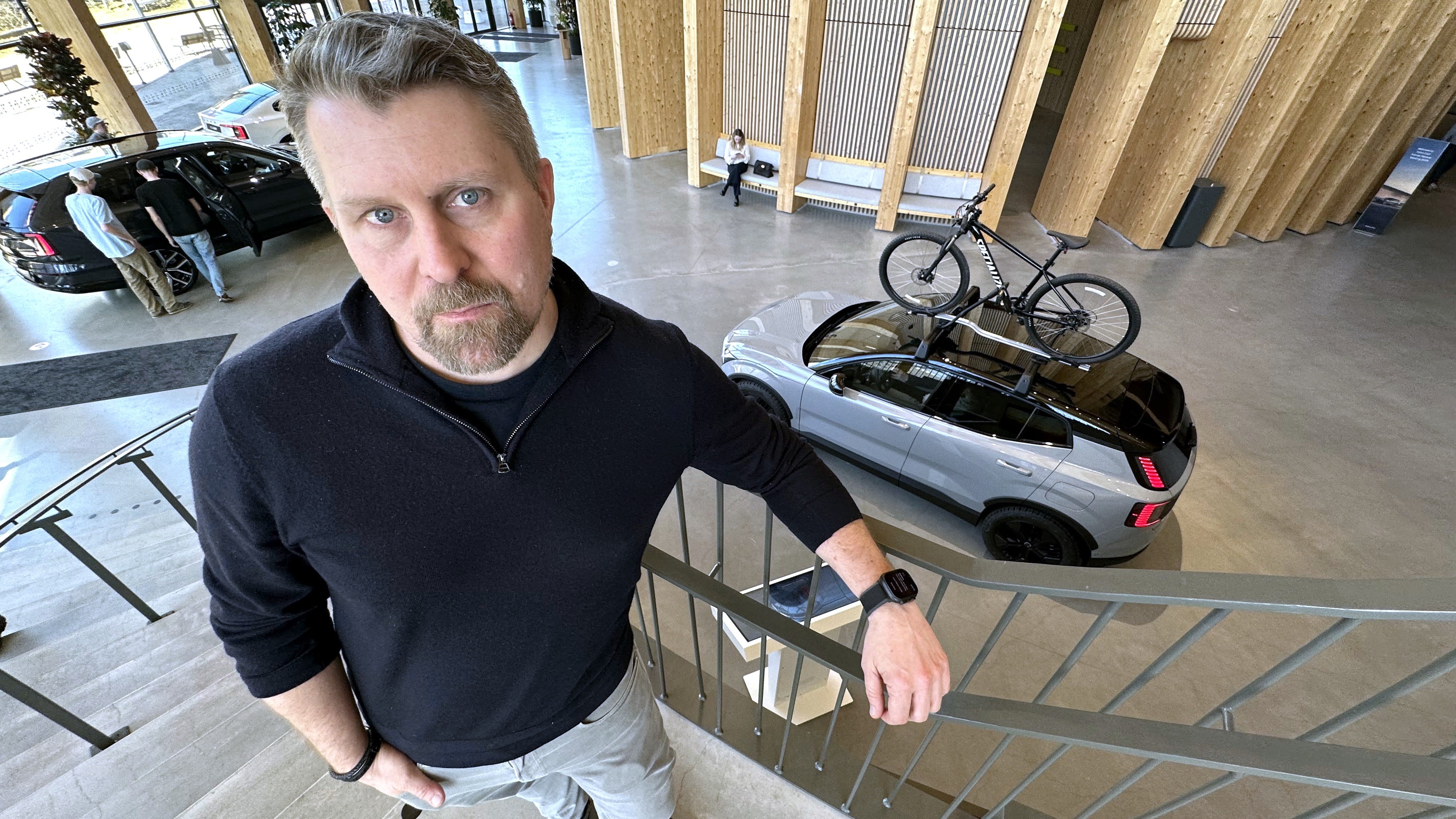 Man i svart tröja står vid en trappa inomhus, med bilar och cyklar synliga i bakgrunden.