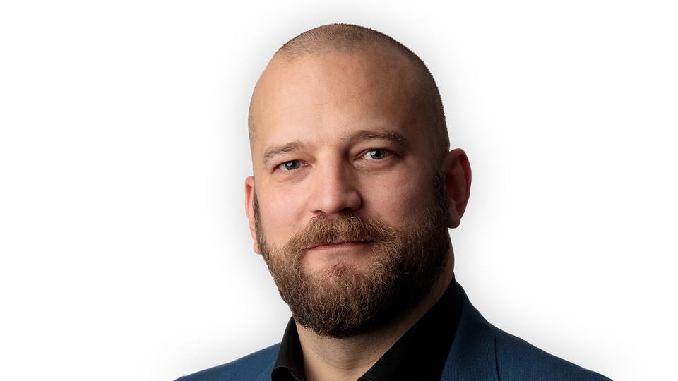 Richard bråse tittar in i kameran. Han ler med stängd mun.